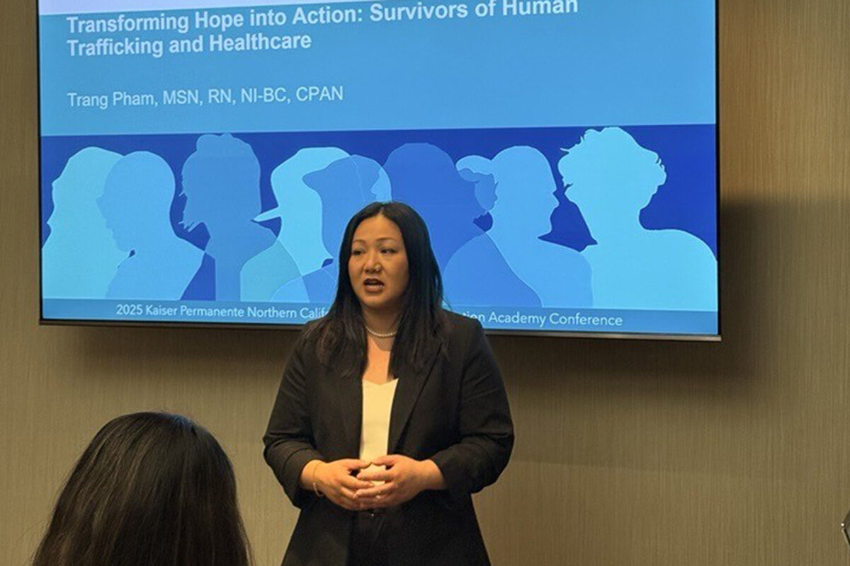 Trang Pham in front of a screen with a presentation on it.