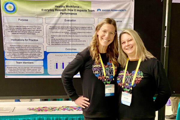 2 Nurses in front of a poster at a conference.