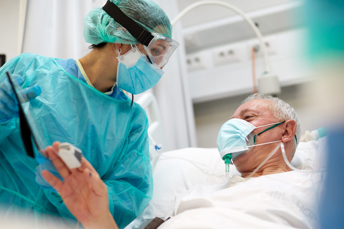 Patient in bed with oxygen mask on speaking to a nurse.