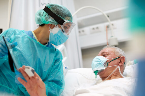 Patient in bed with oxygen mask on speaking to a nurse.