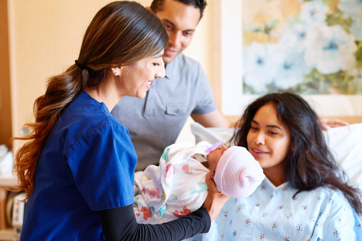 Nurse handing a newborn to mom as dad looks on.