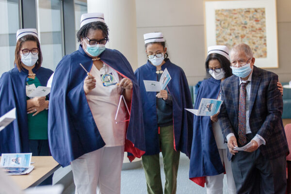 With capes, candles, and comforting words, nurses pay tribute to deceased colleagues. Pictured, Karen Carter, RN, from Vallejo Medical Center, rings a triangle during a memorial at Redwood City Medical center as Janet Sohal, RN, second from right, comforts Jaime Reyes, the husband of the late Leticia Dicioco-Reyes, RN.
