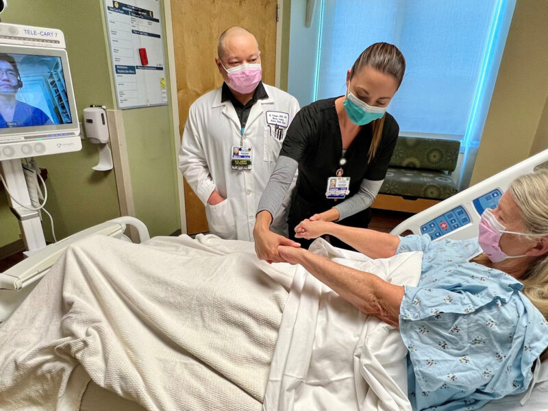 Patient In A Hospital Bed Being Tended To By A Nurse, And Other Medical Professional.