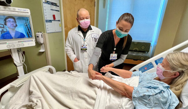 Patient In A Hospital Bed Being Tended To By A Nurse, And Other Medical Professional.