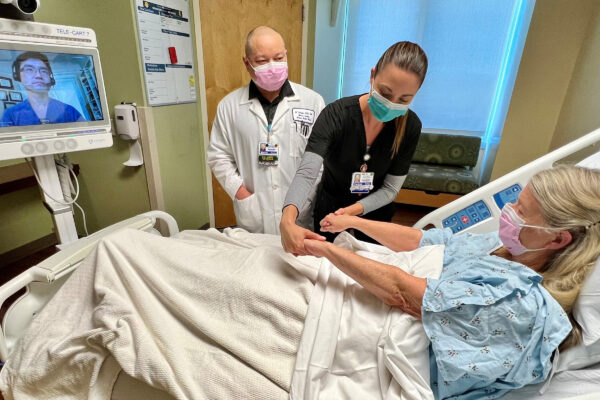Patient in a hospital bed being tended to by a nurse, and other medical professional.