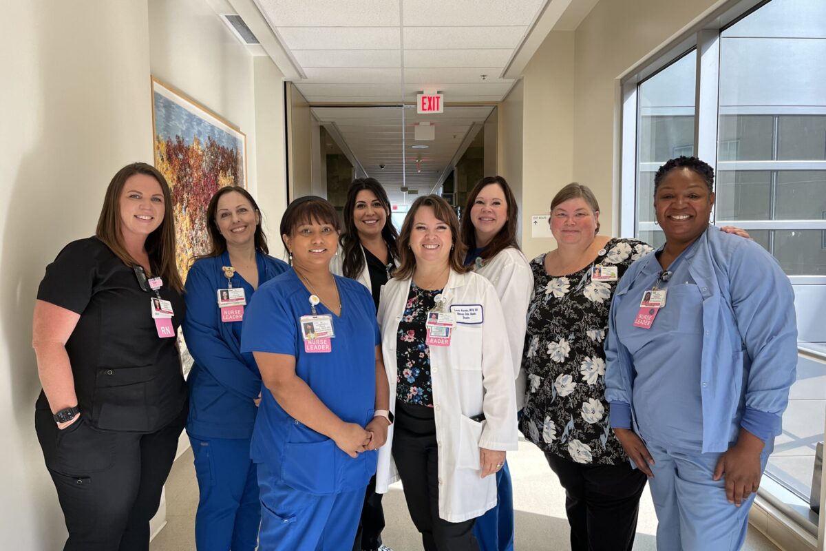 Nursing standing in a hallway smiling.