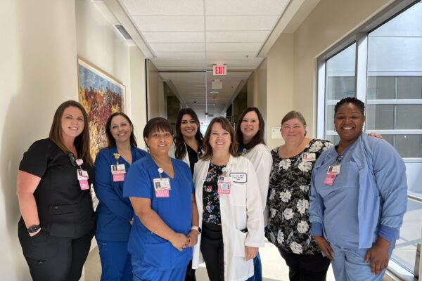 Nursing standing in a hallway smiling.