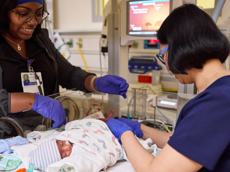 2 nurses in the nicu caring for a baby.