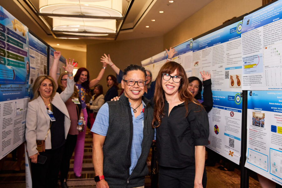 Nurses smiling in front of a series of posters with a group of nurses behind them.