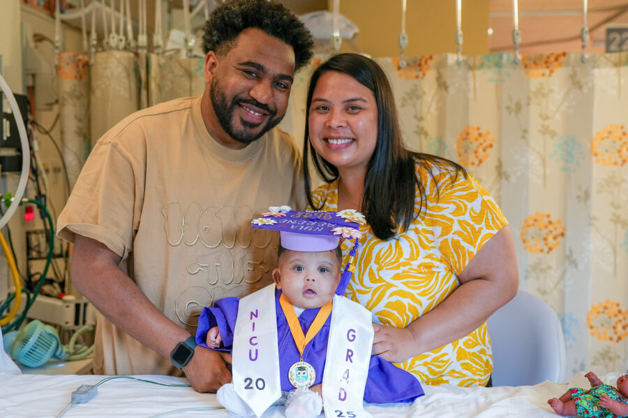 A mom and dad with their infant dressed in a graduation cap and gown.