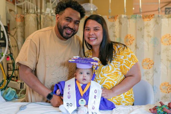 A mom and dad with their infant dressed in a graduation cap and gown.