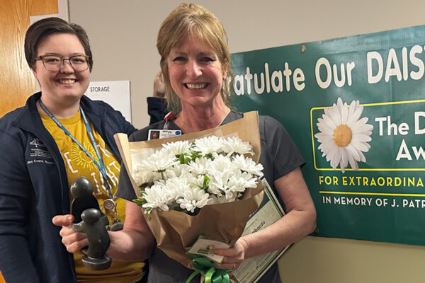 Nurse Rhonda Lombardi holding a bouquet of daisies and a DAISY award.